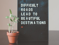 Een motiverende tekst op een bord met een plantje ernaast 